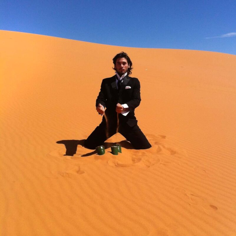 Gio Montez performing ISOLAZIONE in the Sahara Desert, surrounded by sand dunes in a contemplative artistic action exploring solitude and nature